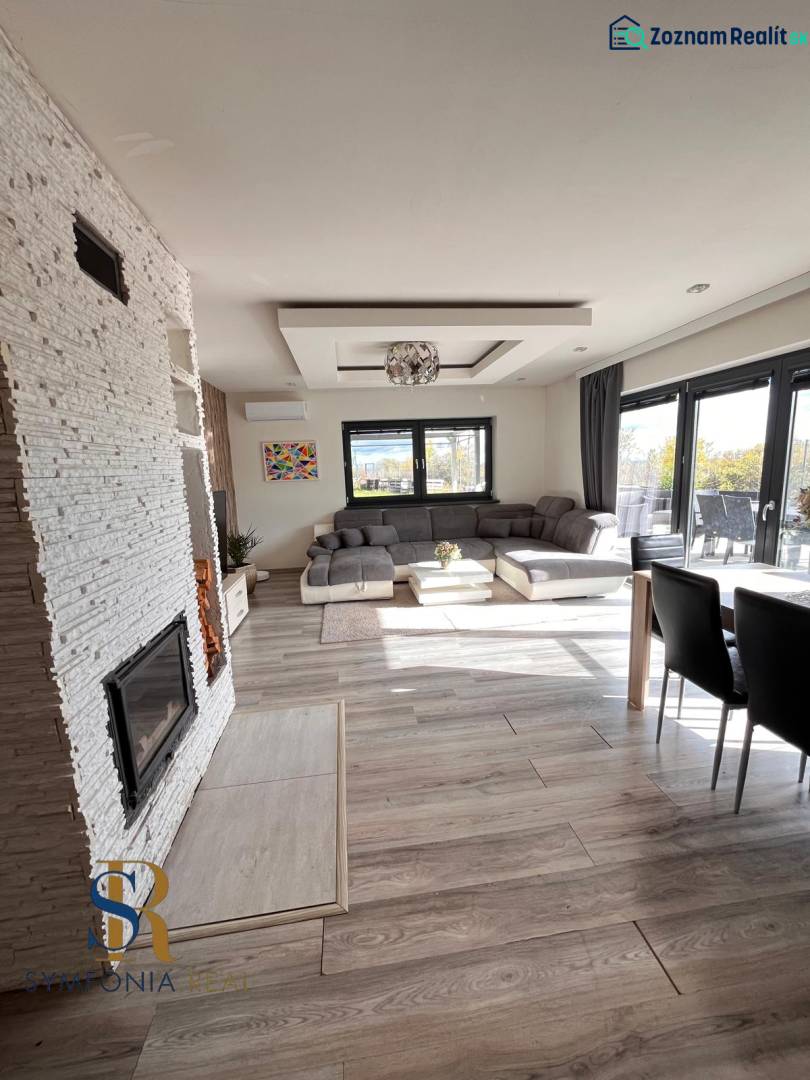 Rodinný dom v obci Dubová s 920m2 rozsiahlym pozemkom  - Interiér rodinného domu s pohovkou, krbom a podlahou s dreveným dekorom.