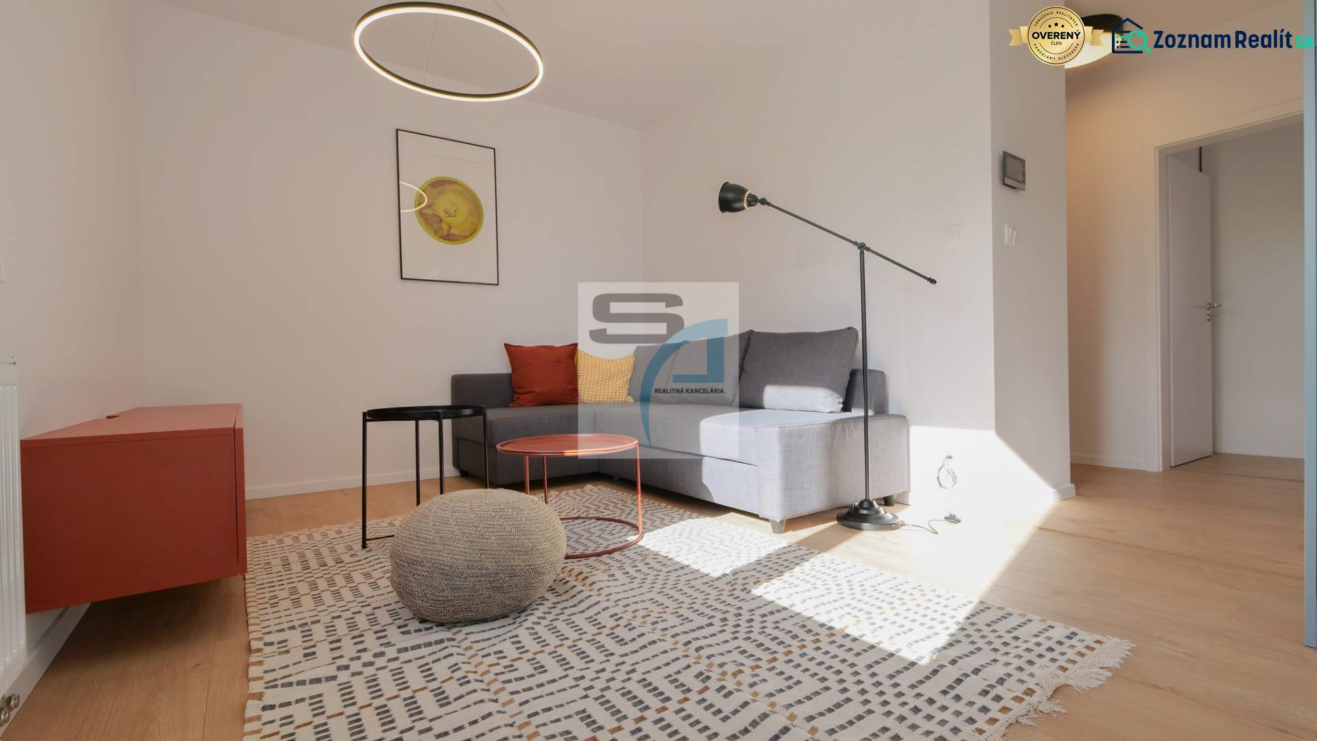 2-izbový byt s terasou 15 m² a parkovaním v tichej časti Bratislavy - Obývačka v 2-izbovom byte s podlahou s dreveným dekorom, sivou sedačkou a moderným osvetlením.