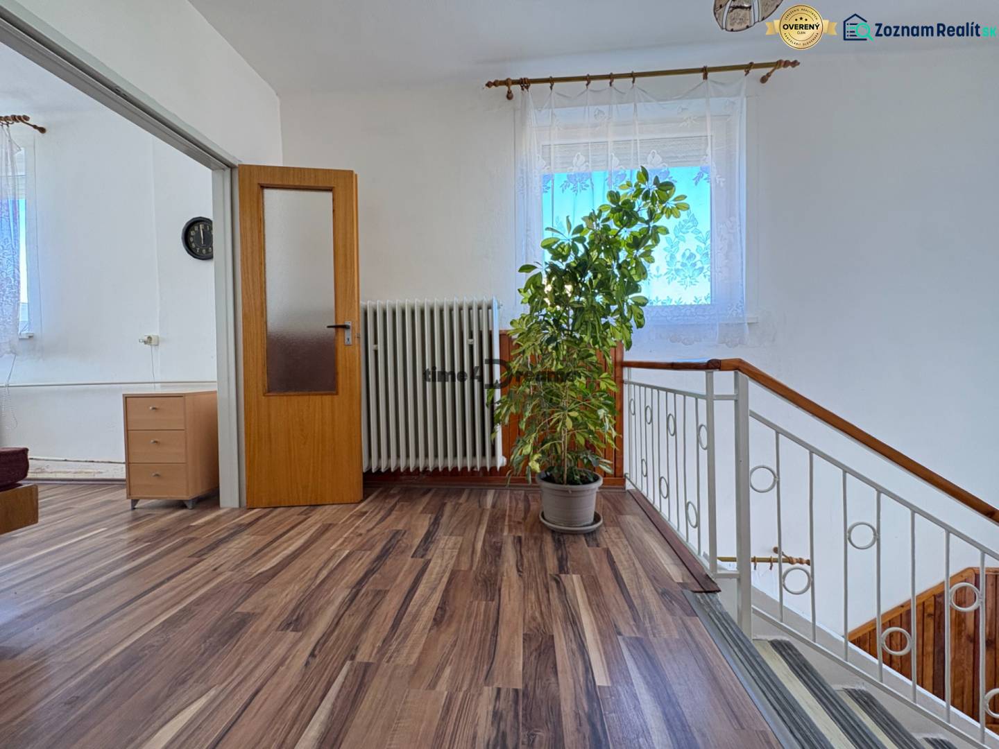 Na predaj: Rodinný dom v meste Levice - Interiér rodinného domu s podlahou s dreveným dekorom, veľkou rastlinou a zábradlím schodiska.