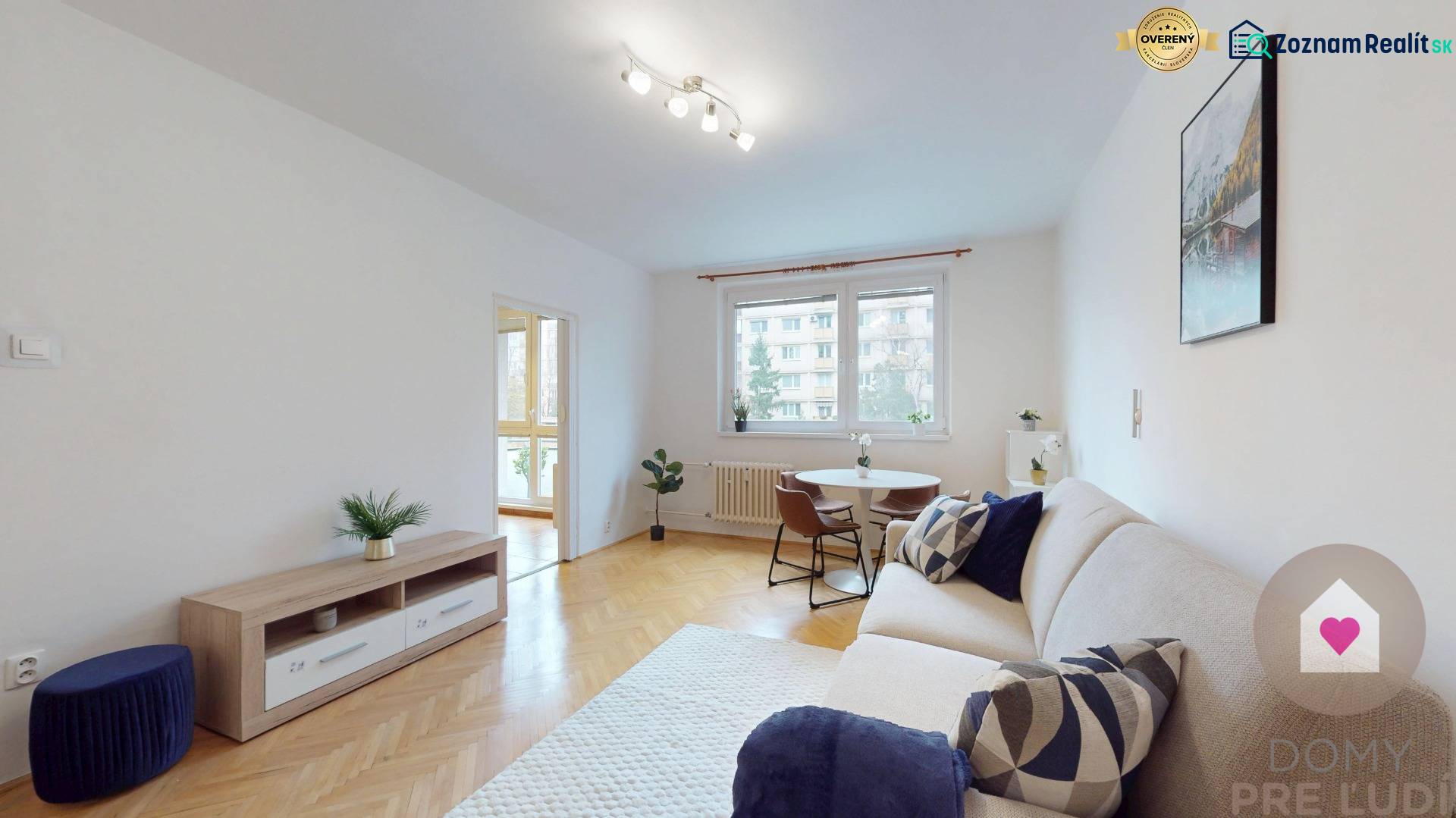 BA/RUŽINOV-Prenájom 1i bytu s balkónom a pivnicou v skvelej lokalite - Obývačka 1-izbového bytu s podlahou s dreveným dekorom, gaučom a okrúhlym stolom.