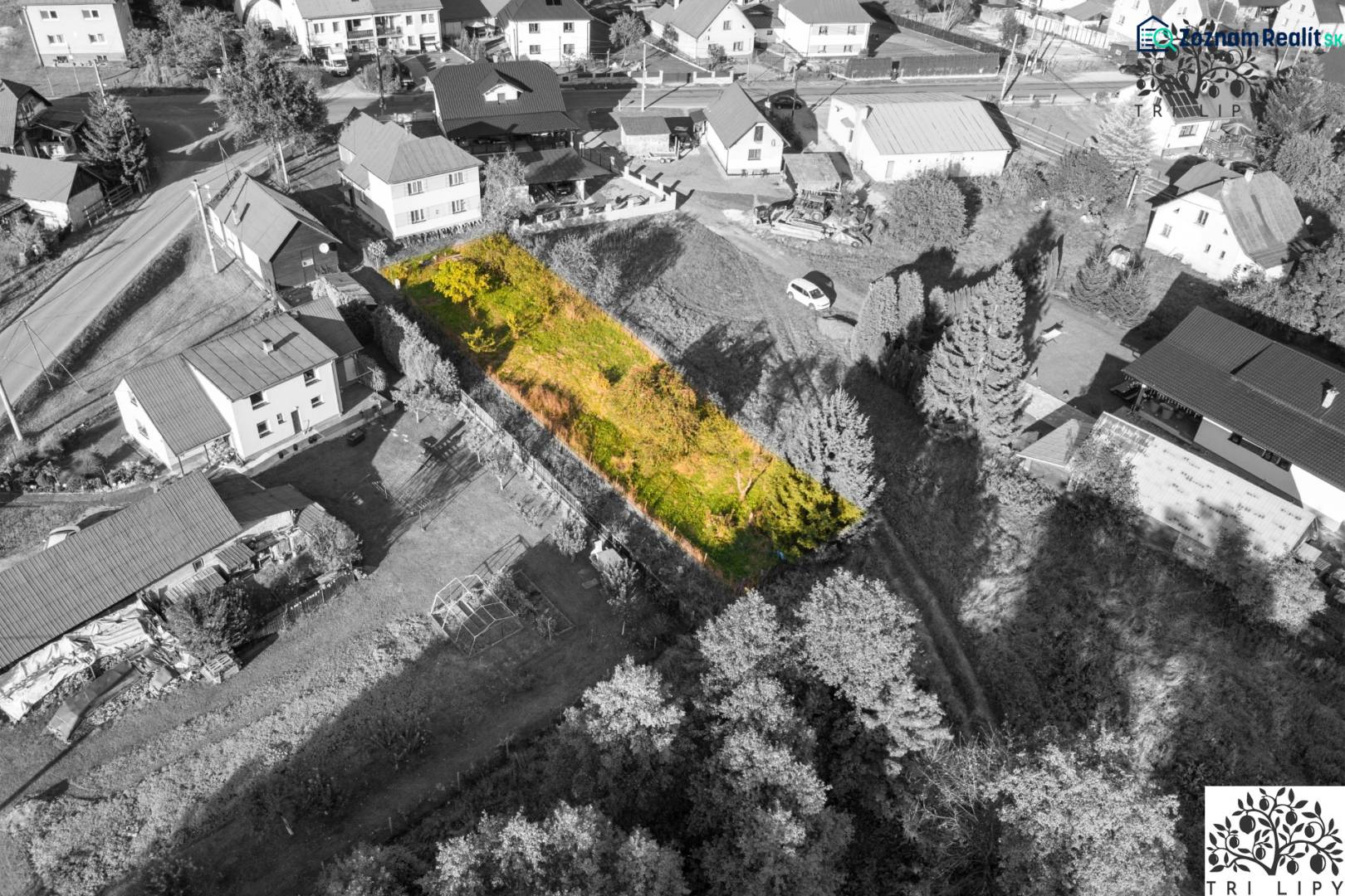 Stavebný pozemok - Turzovka - stavebné povolenie - Pozemok na bývanie v Turzovke, obklopený domami, s trávnatým porastom a stromami.