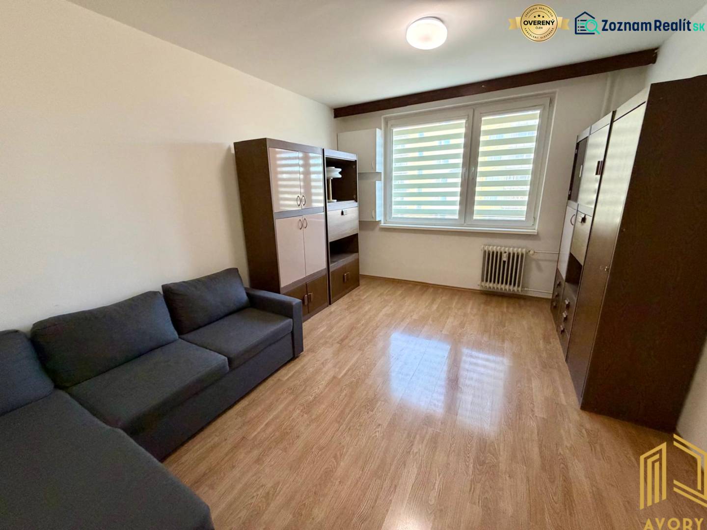 NA PREDAJ 1-IZBOVÝ BYT (37m2), SENICA, HVIEZDOSLAVOVA UL. - Obývacia izba v 1-izbovom byte s podlahou s dreveným dekorom, pohovkou a skrinkami.