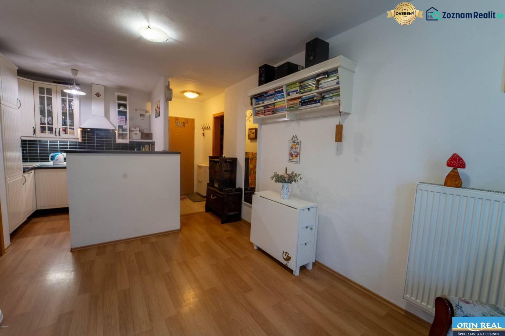 Na predaj útulný 2 izbový byt so zahradkou Svätý Jur 165.000,- Eur - Interiér 2-izbového bytu s kuchyňou, police s knihami, podlaha s dreveným dekorom.