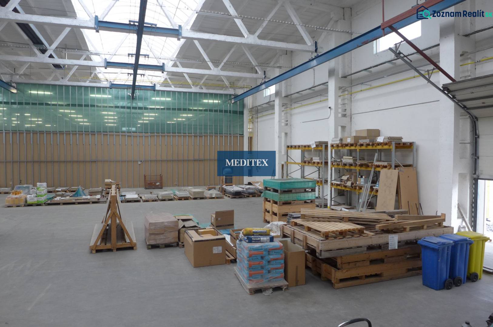 Sklad na prenájom o celkovej ploche 1015 m2 - V sklade sú palety so stavebným materiálom a regály s uloženými doskami.