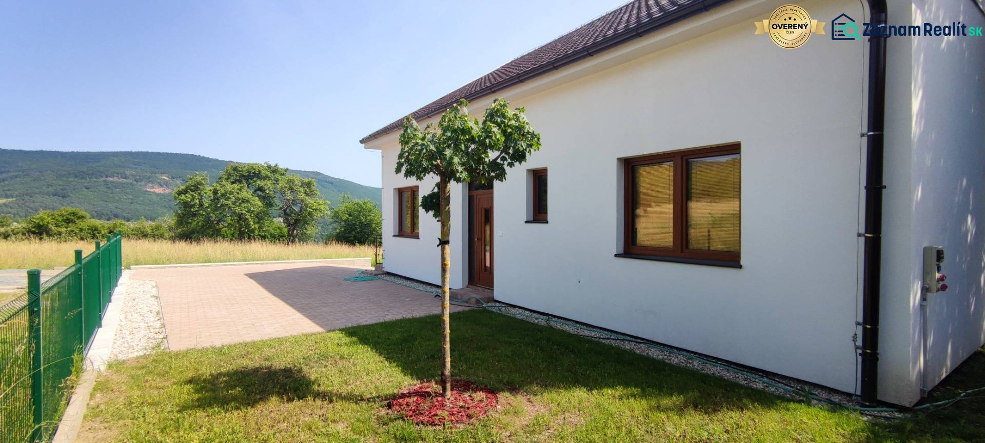 Predaj novostavba rodinného domu   Nová Baňa - Rodinný dom v Novej Bani s trávnikom, stromom a dlažbou, obklopený prírodou.