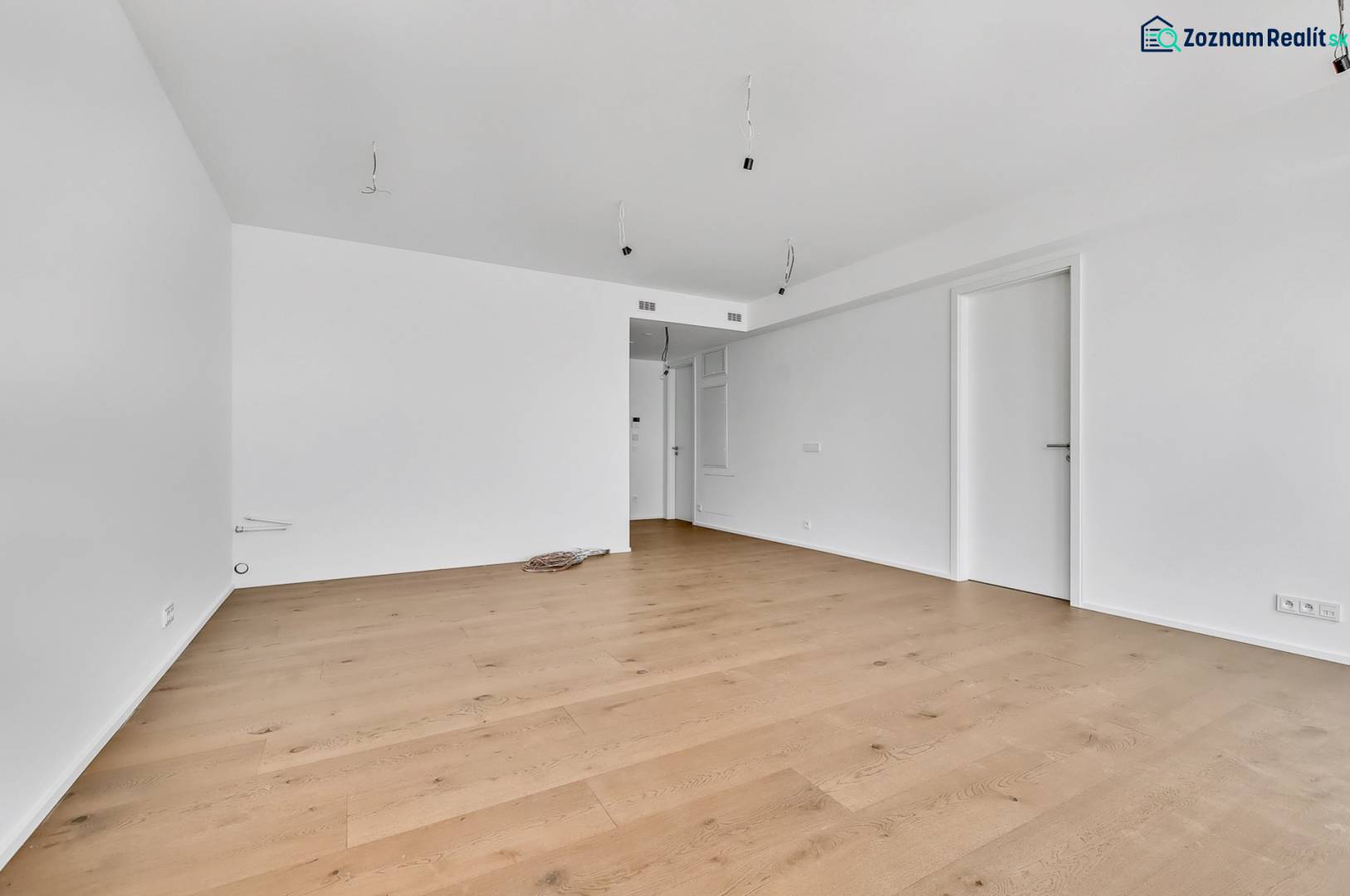 PREDAJ - LIGET Nový 2 izbový apartmán pri Sade Janka Kráľa, Petržalka - Prázdna izba s drevenou podlahou a bielymi stenami v 2-izbovom byte.