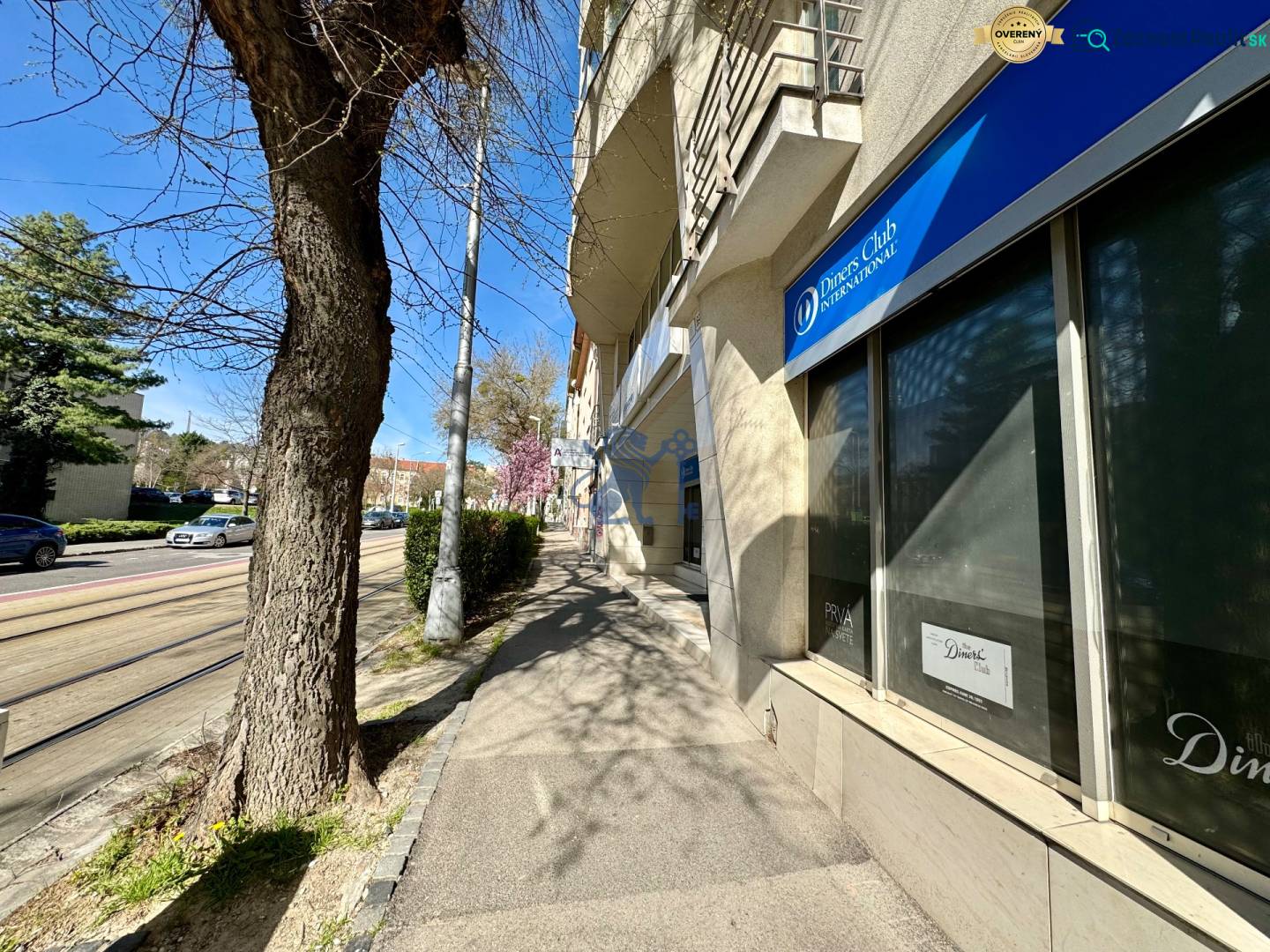 Obchodno- kancelársky priestor s výkladom na Nám. slobody - Budova na ulici Námestie slobody, kancelárie a hlavná cesta, slnečný deň, zaparkované autá.