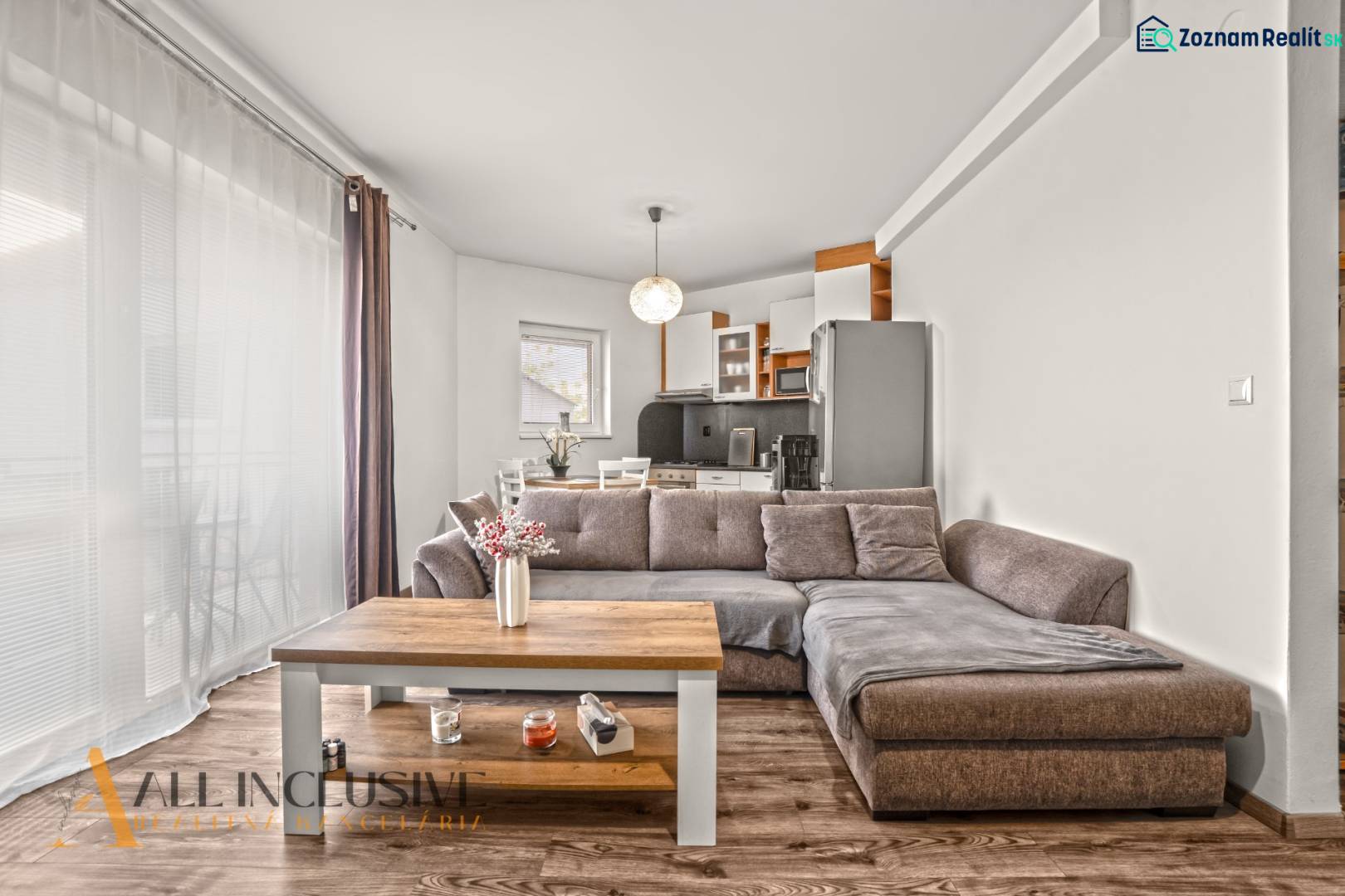 NA PREDAJ 2-IZBOVÝ BYT S 2 BALKÓNMI, DUNAJSKÁ STREDA - Obývačka v 2-izbovom byte so sedačkou, kuchynskou linkou a podlahou s dreveným dekorom.