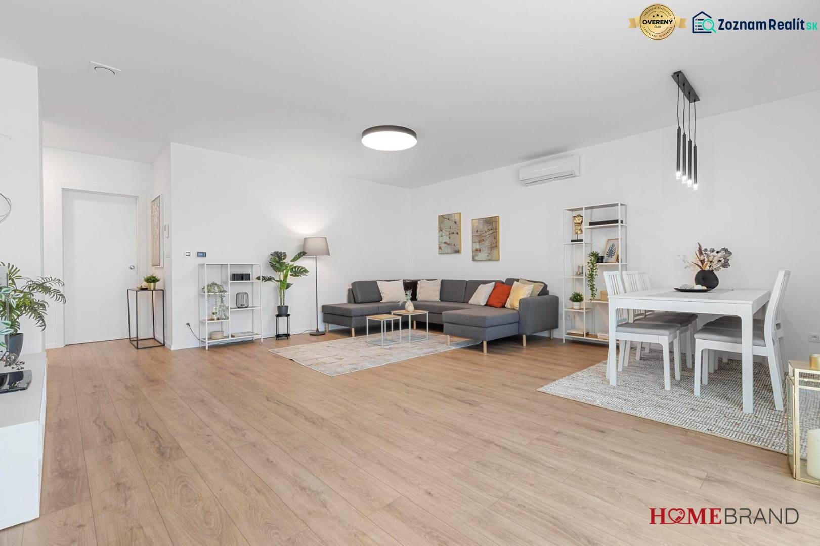 BÝVANIE VO VILA DOME - POSLEDNÝ VOĽNÝ 3-IZBOVÝ BYT SO ZÁHRADOU - Priestranná obývacia izba s podlahou s dreveným dekorom a sedačkou v 3-izbovom byte.