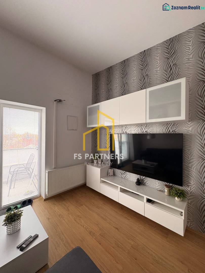 Prenájom moderného 2-izbového bytu v centre Komárna, 40 m² – Petőfiho  - Obývacia izba s TV stenou, vzorovanou tapetou a podlahou s dreveným dekorom v 2-izbovom byte.