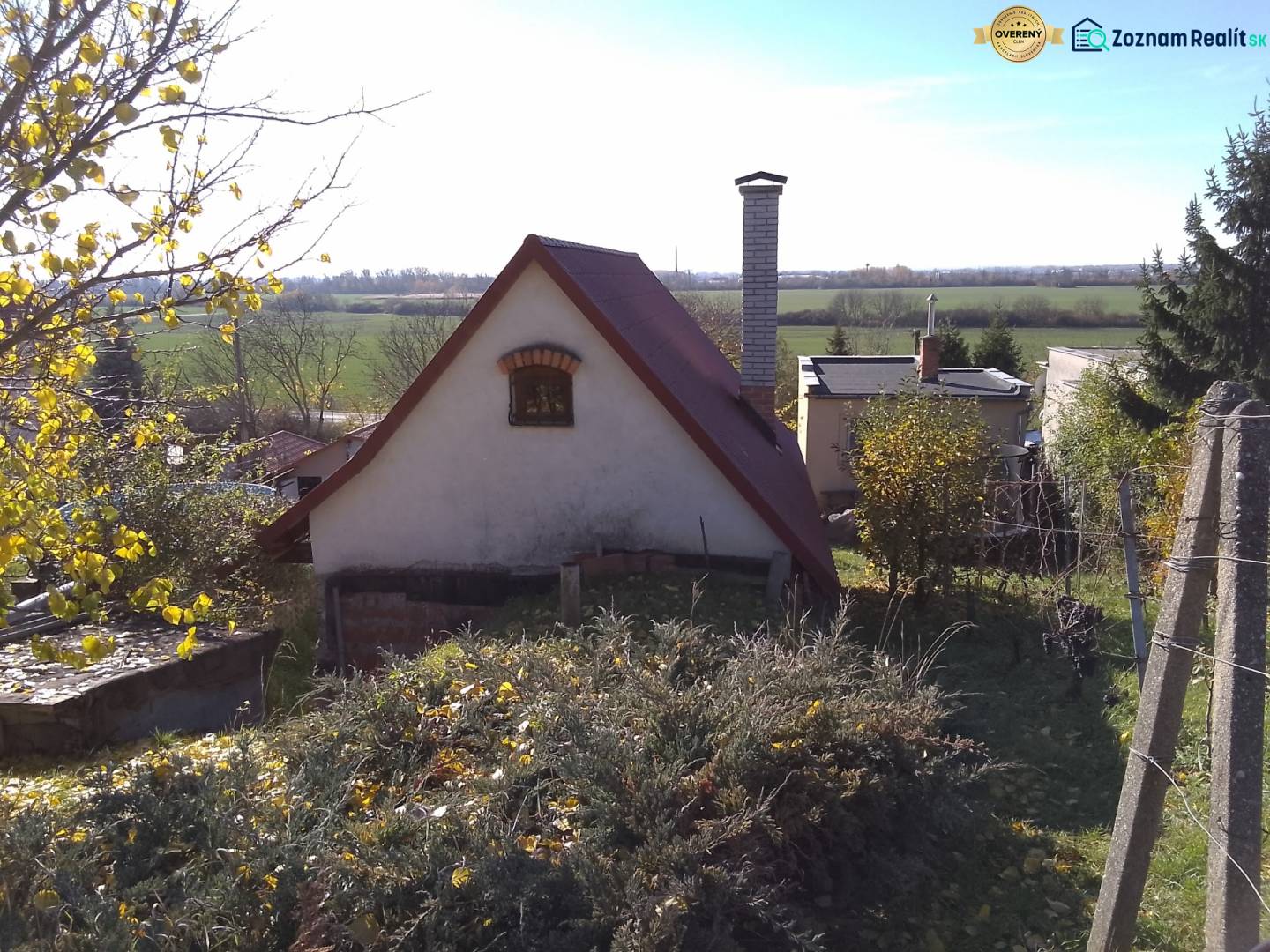 Štýlový rekreačný domček Levice - Chata v Starých Leviciach, rekreačná lokalita, obklopená prírodou a kríkmi, v pozadí pole.