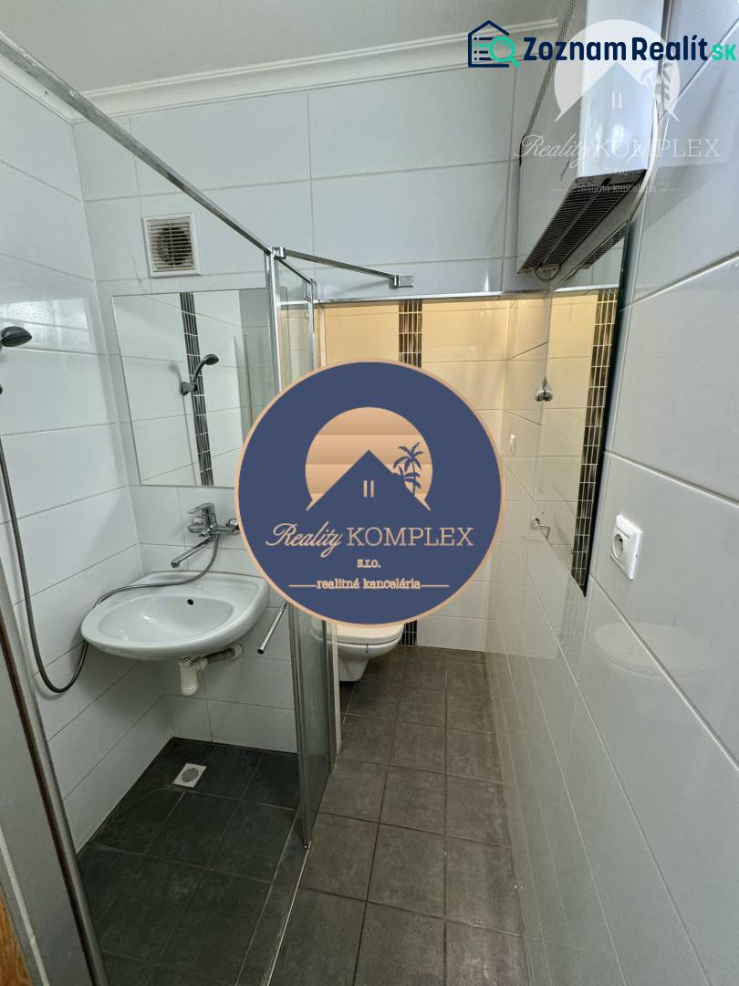 Vám ponúka 1 izbový byt vo VYHĽADÁVANEJ lokali - Kúpeľňa so sprchovým kútom a tmavou podlahou v 1-izbovom byte, biele obklady.