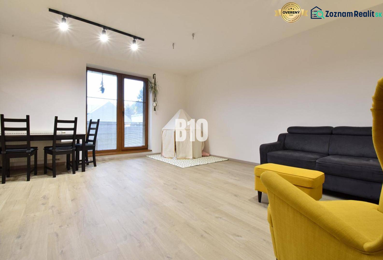 Veľkometrážny 3 izbový byt s garážou - Obývačka v 3-izbovom byte s podlahou s dreveným dekorom a žltým kreslom.