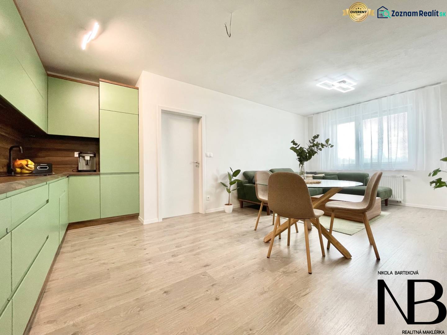 Na predaj štýlový 2-izbový byt s loggiou a parkovaním – TN, Na Pažiti - Obývačka v 2-izbovom byte s podlahou s dreveným dekorom a zelenou kuchyňou.
