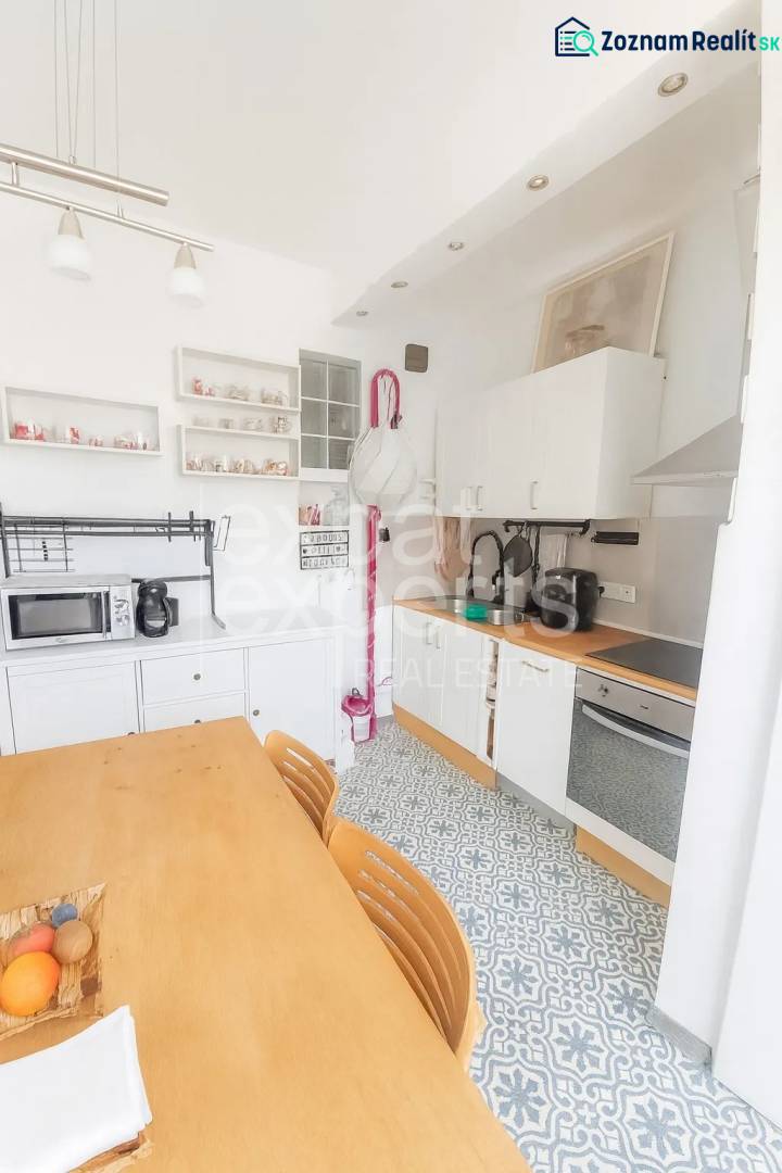 Svetlý, jedinečný 2i byt 62m2, po rekonštrukcií, s pivnicou   - Kuchyňa v 3-izbovom byte s jedálenským stolom, vzorovanou podlahou a bielymi skrinkami.