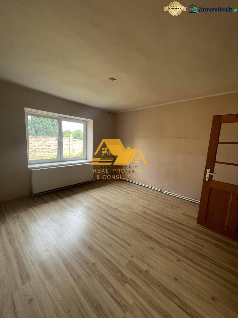 Exkluzívne! Predám rodinný dom v obci Svodín - Izba s veľkým oknom a podlahou s dreveným dekorom v rodinnom dome.