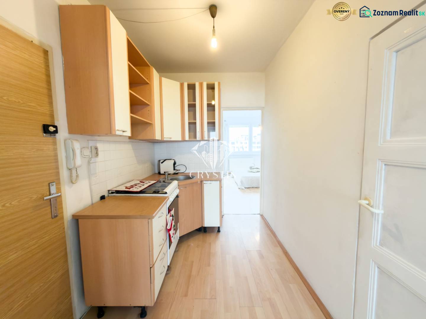 Na predaj 2,5- izbový byt Žilina-Solinky - Kuchyňa v 2-izbovom byte s podlahou s dreveným dekorom a bielymi skrinkami.