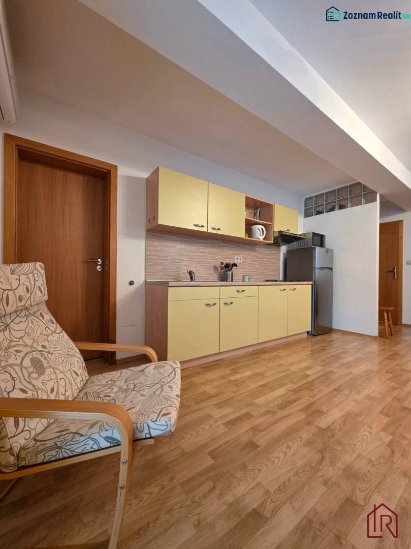 Apartmán, Nová Lesná, 46m2 + balkón, park. miesto, zariadený  - Rekreačný apartmán s kuchynskou linkou, kreslom a podlahou s dreveným dekorom.