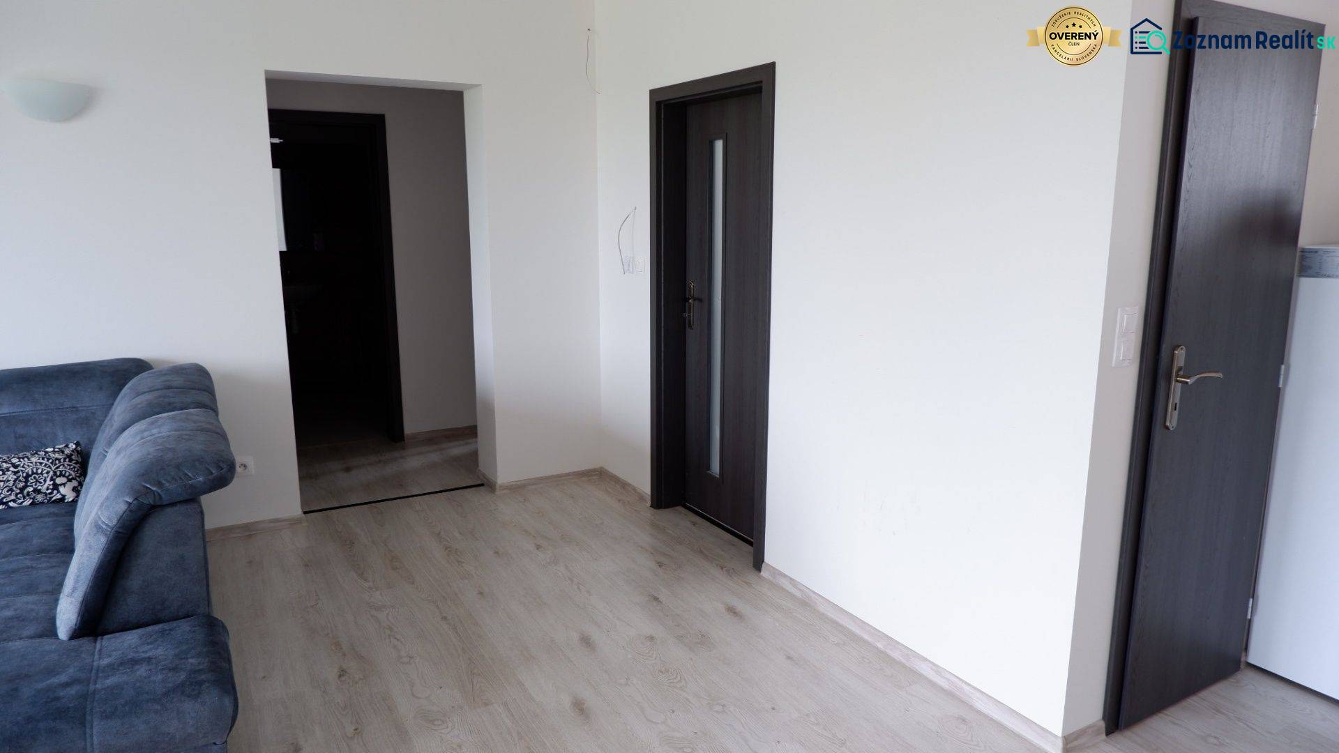 Ponúkame na predaj 3 izbový radový dom v obci Rastislavice. - Interiér rodinného domu s pohovkou, podlahou s dreveným dekorom a tmavými dverami.