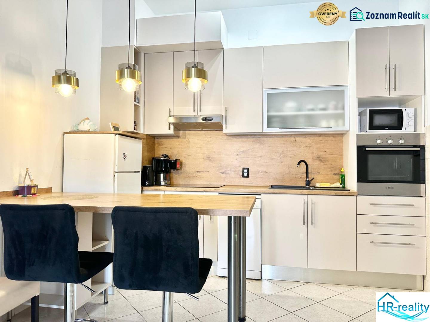 Trogir, Čiovo – pekný, zariadený apartmán len 150m od pláže - Kuchyňa v rekreačnom apartmáne s barovým pultom, závesnými svietidlami a bielou skríňou.