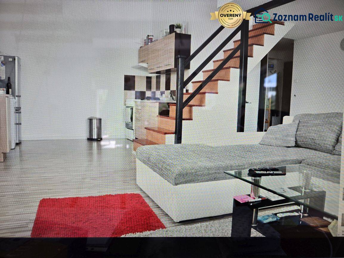 Na predaj ubytovňa / rodinný dom  v Šali  Veči s kapacitou 50 osôb - Obývacia izba s kuchynským kútom, schodiskom, gaučom, skleneným stolíkom a podlahou s dreveným dekorom.