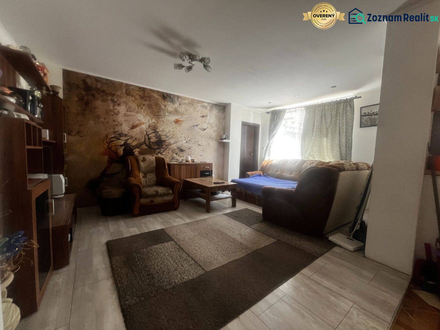 Rodinný dom s prístavbou na  podnikanie – Tešedíkovo - Obývacia izba v rodinnom dome s pohovkou, kreslami a nástennou maľbou za sedením.