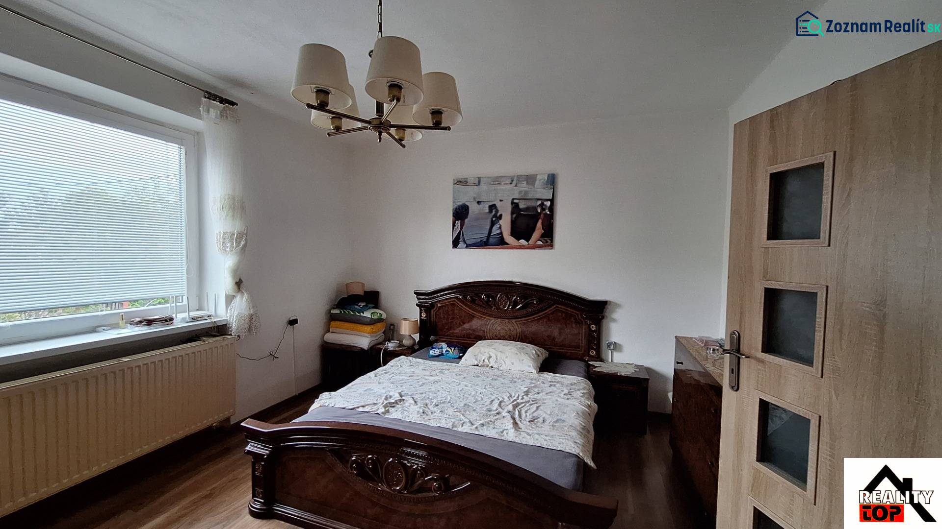 Investujte do budúcnosti - Spálňa v rodinnom dome s posteľou, lustrom a podlahou s dreveným dekorom.