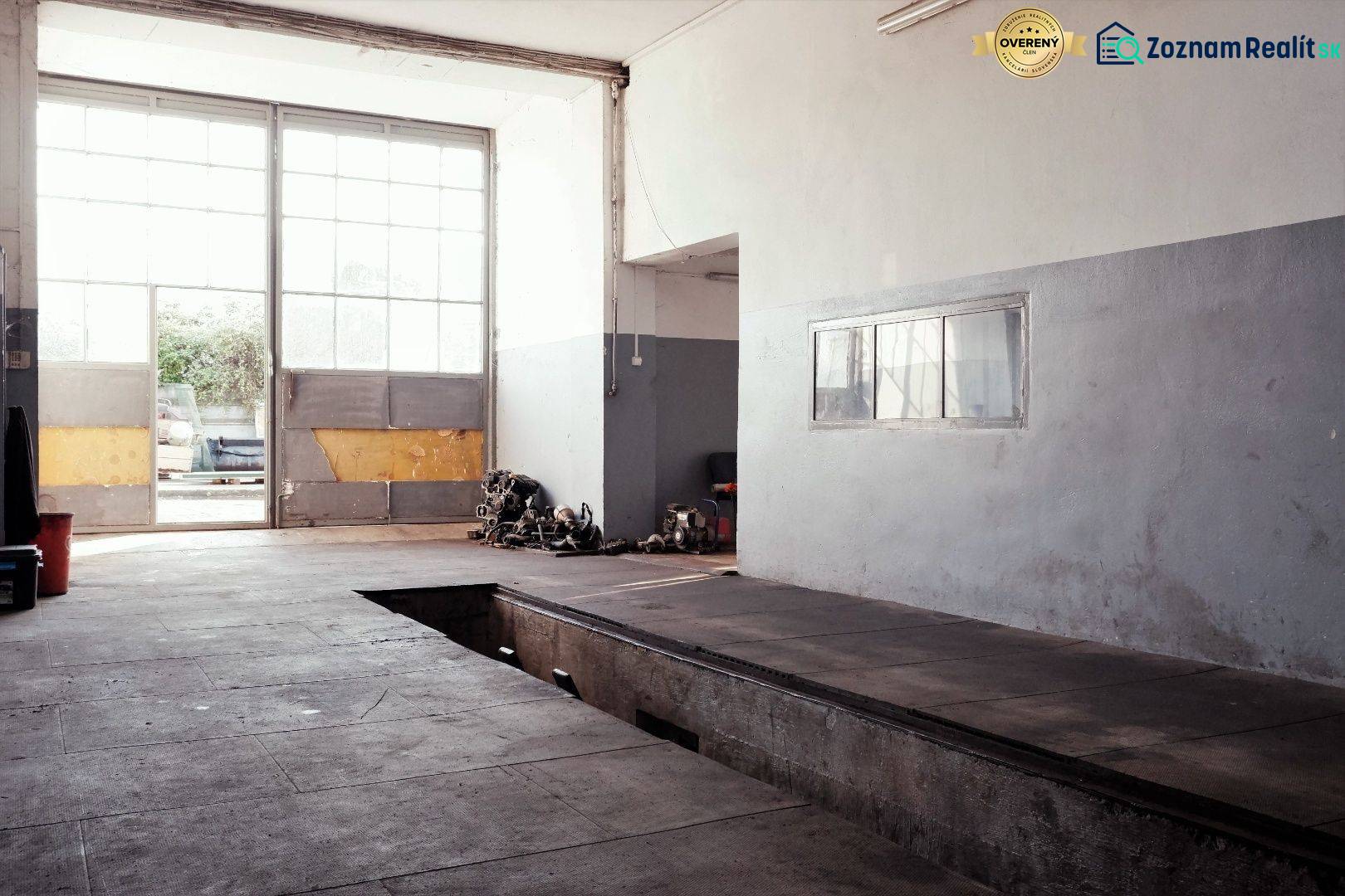Prevádzková budova-AUTOSERVIS na predaj vo Veľkých Úľanoch - Výrobné priestory s veľkými oknami, garážovou bránou a podlahou s dreveným dekorom.