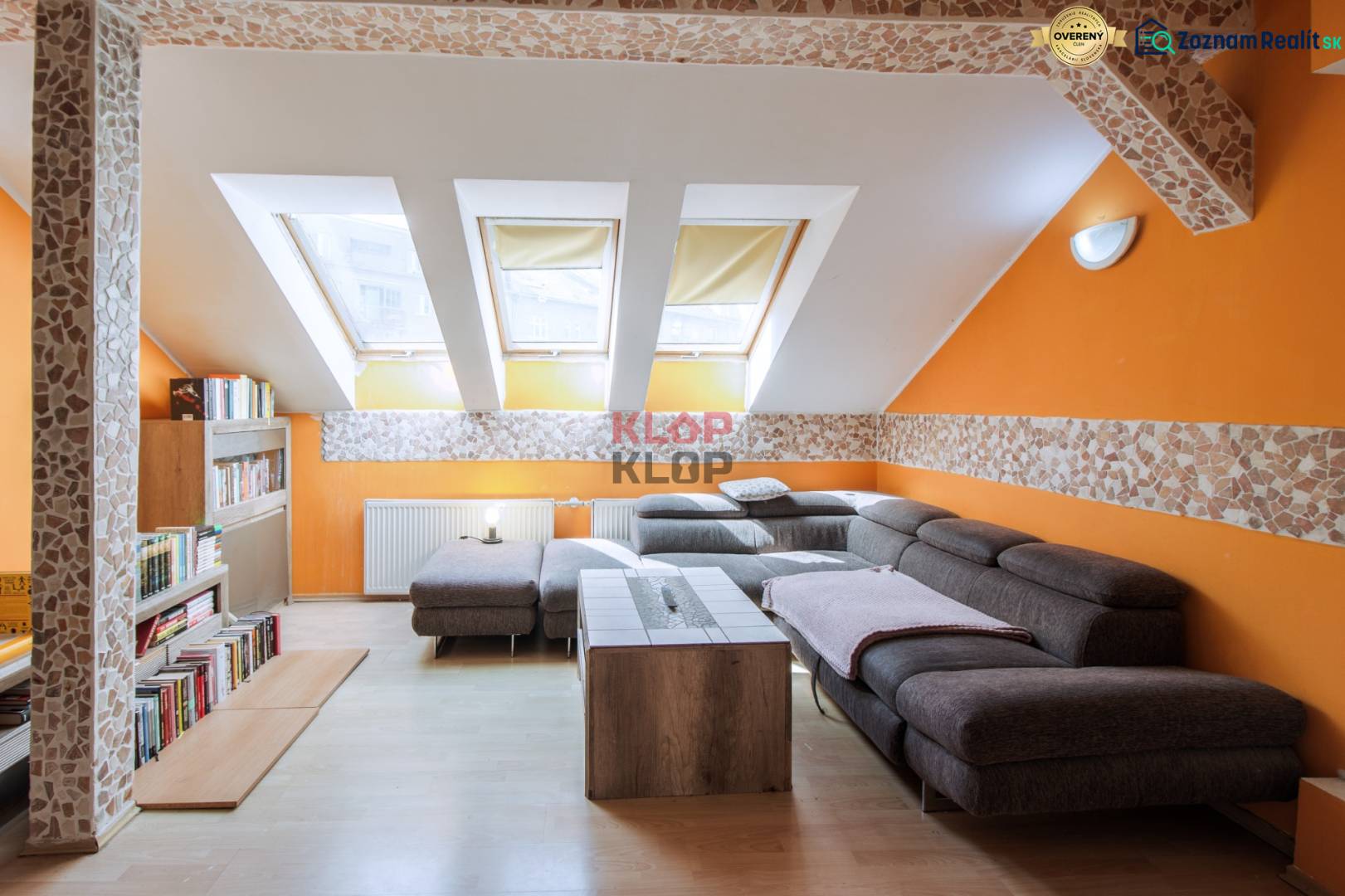 Kúpte si veľký PODKROVNÝ 4i BYT so ZÁHRADOU a PIVNICOU v Starom meste - Podkrovná obývačka s oranžovými stenami, šedou sedačkou a knižnicou v 4-izbovom byte.