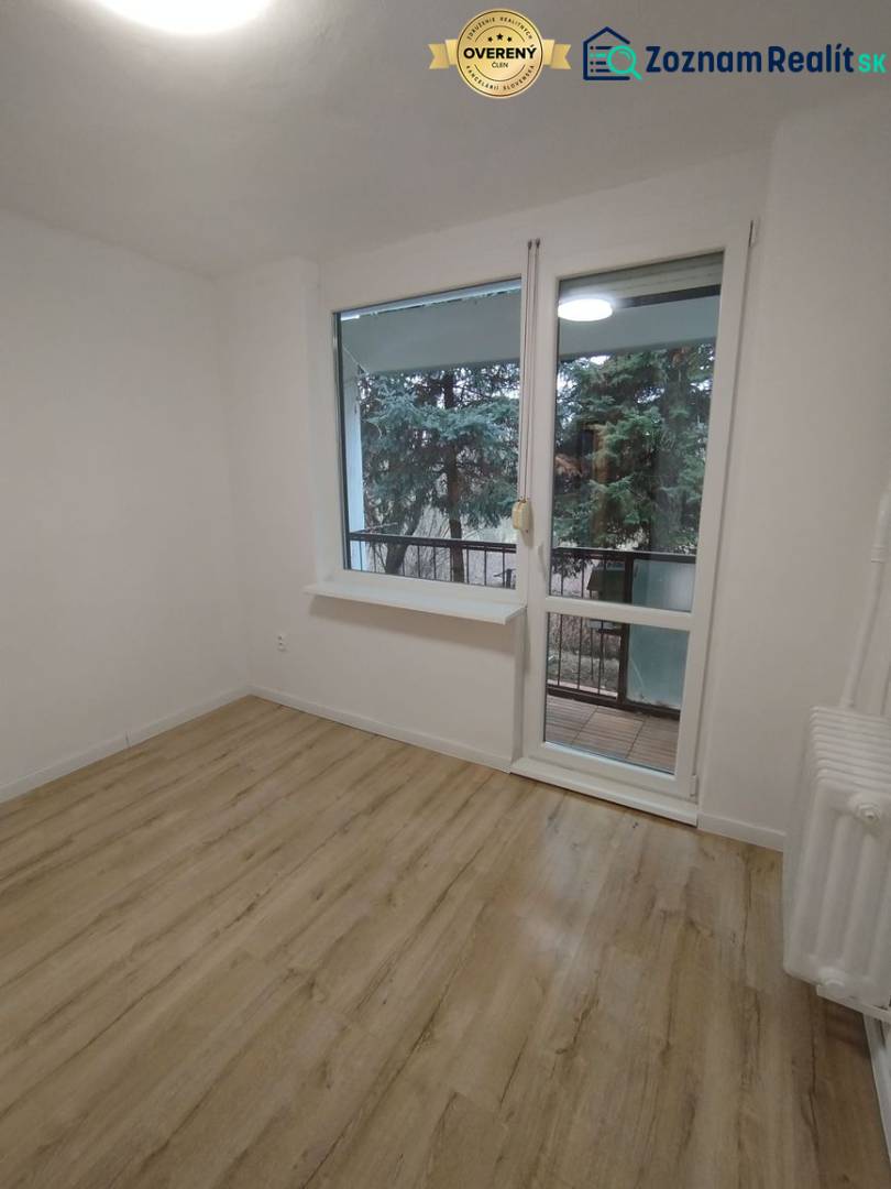  Na predaj  3i byt s vlastnou garážou neďaleko Šale - Izba so svetlými stenami, podlahou s dreveným dekorom a výhľadom na zeleň.