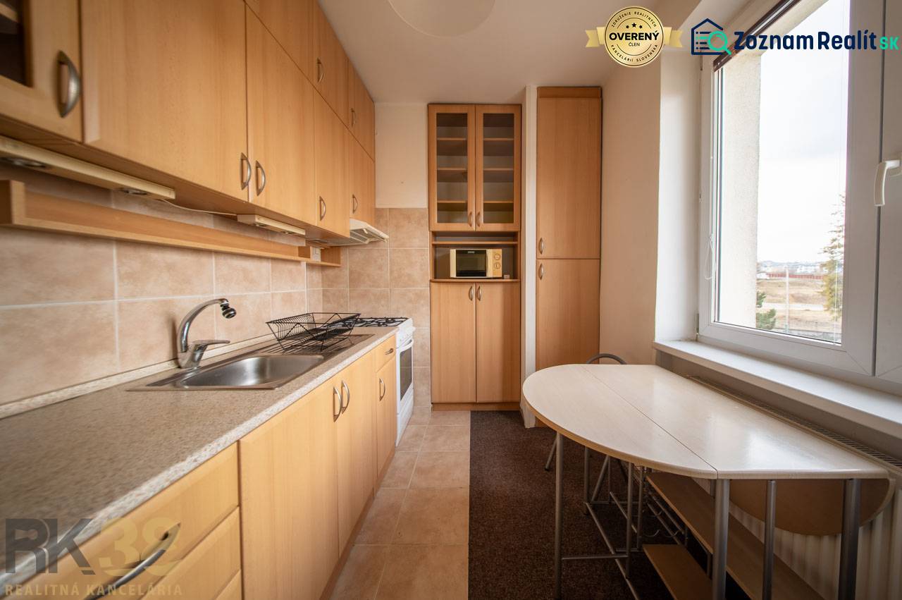 Rezervované: Na predaj pekný 2-izbový byt v centre mesta Poprad - Kuchyňa v 2-izbovom byte s podlahou s dreveným dekorom, svetlým nábytkom a stolom pri okne.