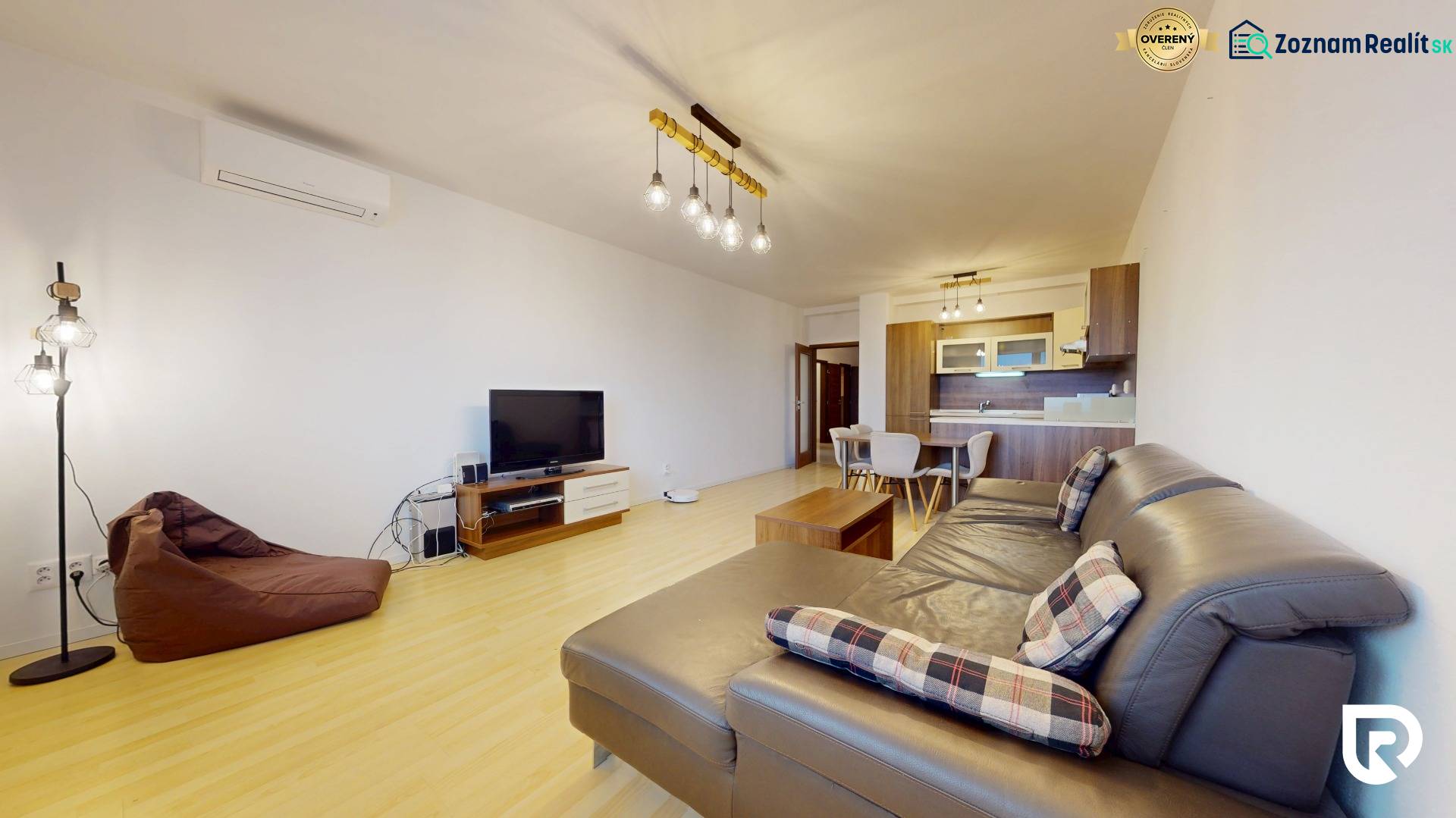 | Svetlý priestranný 2 izbový byt | parkovanie | REZERVOVANÝ - Obývačka 2-izbového bytu s podlahou s dreveným dekorom, veľkou sedačkou a televíziou.