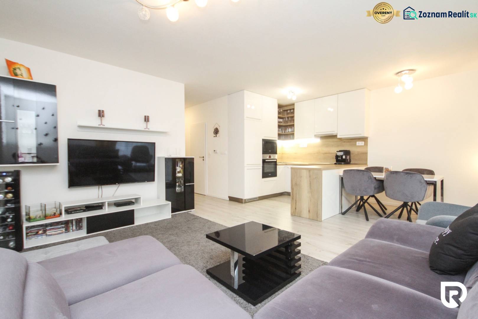 3i byt + záhradka 94m2 + parking, Vinohrady, Trenčín - Obývacia izba s kuchyňou v 3-izbovom byte, pohodlné sedenie, televízor, jedálenský stôl.