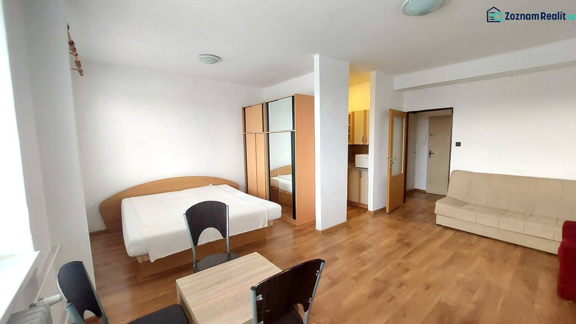 Slnečný 1 izb. byt Piešťany, praktická poloha, kúpou voľný - 1-izbový byt s podlahou s dreveným dekorom, posteľou, gaučom a skriňou.