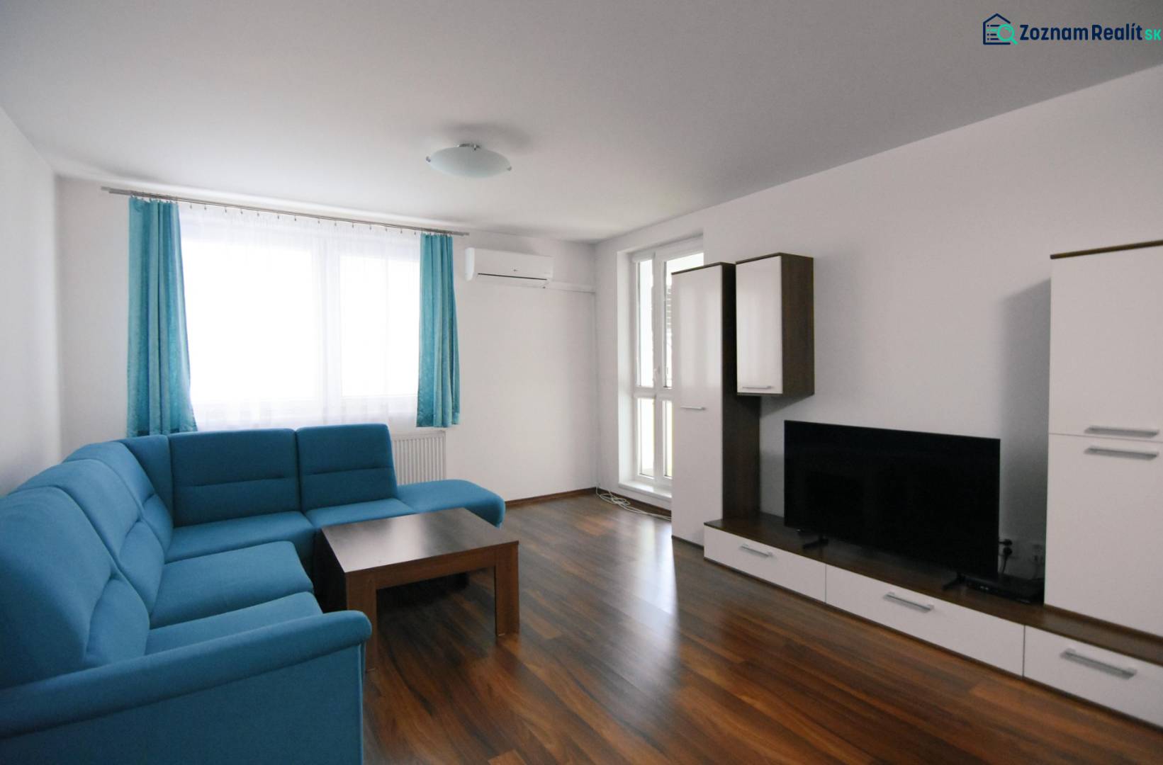 2 izbový byt na prenájom Dolný Šianec, Trenčín - Obývacia izba v 2-izbovom byte s modrým gaučom a podlahou s dreveným dekorom.