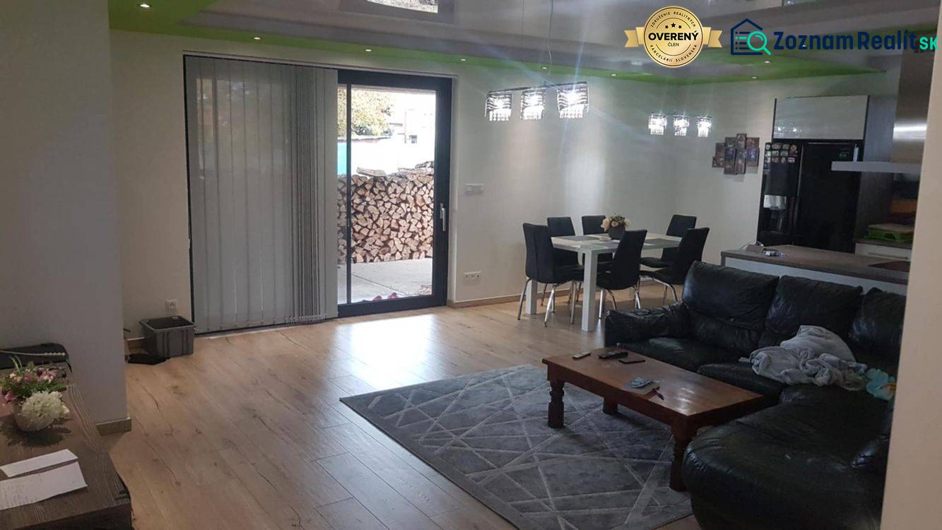 Predaj 4-izbového rodinného domu s veľkou záhradou v Semerove - Obývačka v rodinnom dome s podlahou s dreveným dekorom, pohovkou a jedálenským stolom.