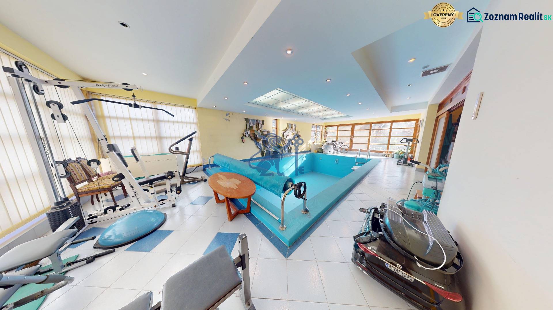Veľkometrážny dom s wellness, bazénom a investičným potenciálom - Interiér rodinného domu s bazénom a posilňovacími strojmi, svetlé priestory s veľkými oknami.
