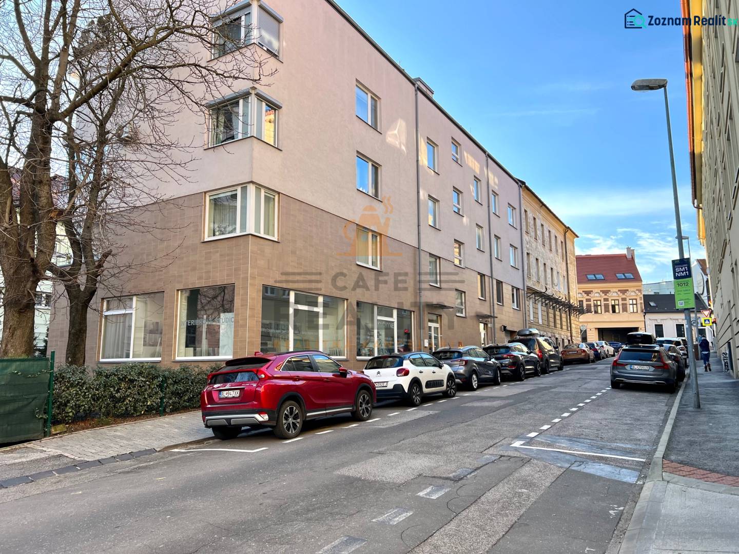 Na predaj parkovacie miesto, Beskydská, Bratislava, Staré Mesto - Ulica s autami, budovami, stromami, v pozadí modrá obloha a zaparkované garáže.