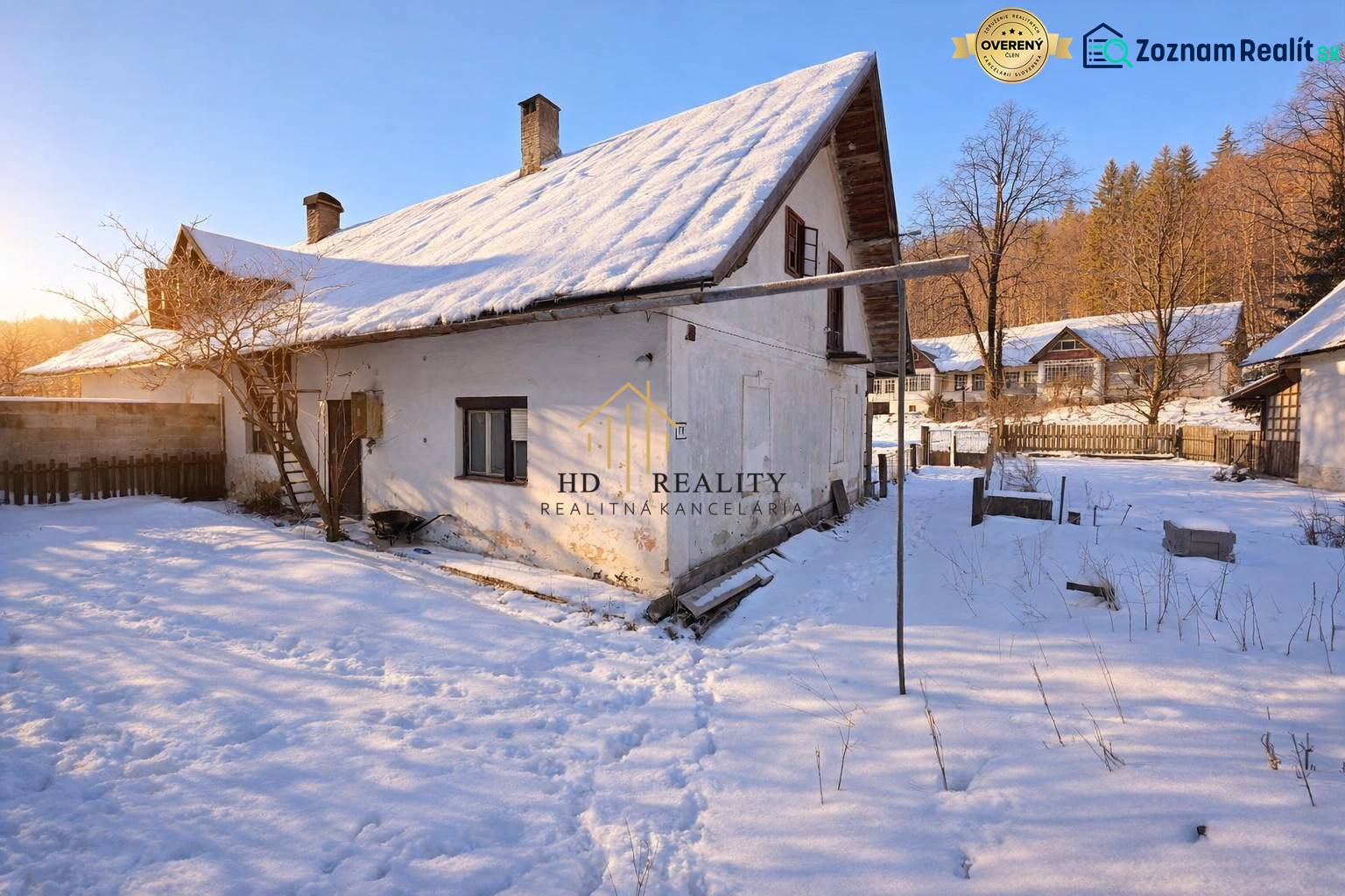 Predaj, rodinný dom Sliačany, Donovaly - Zasnežený rodinný dom v Donovaloch obklopený stromami a modrou oblohou.
