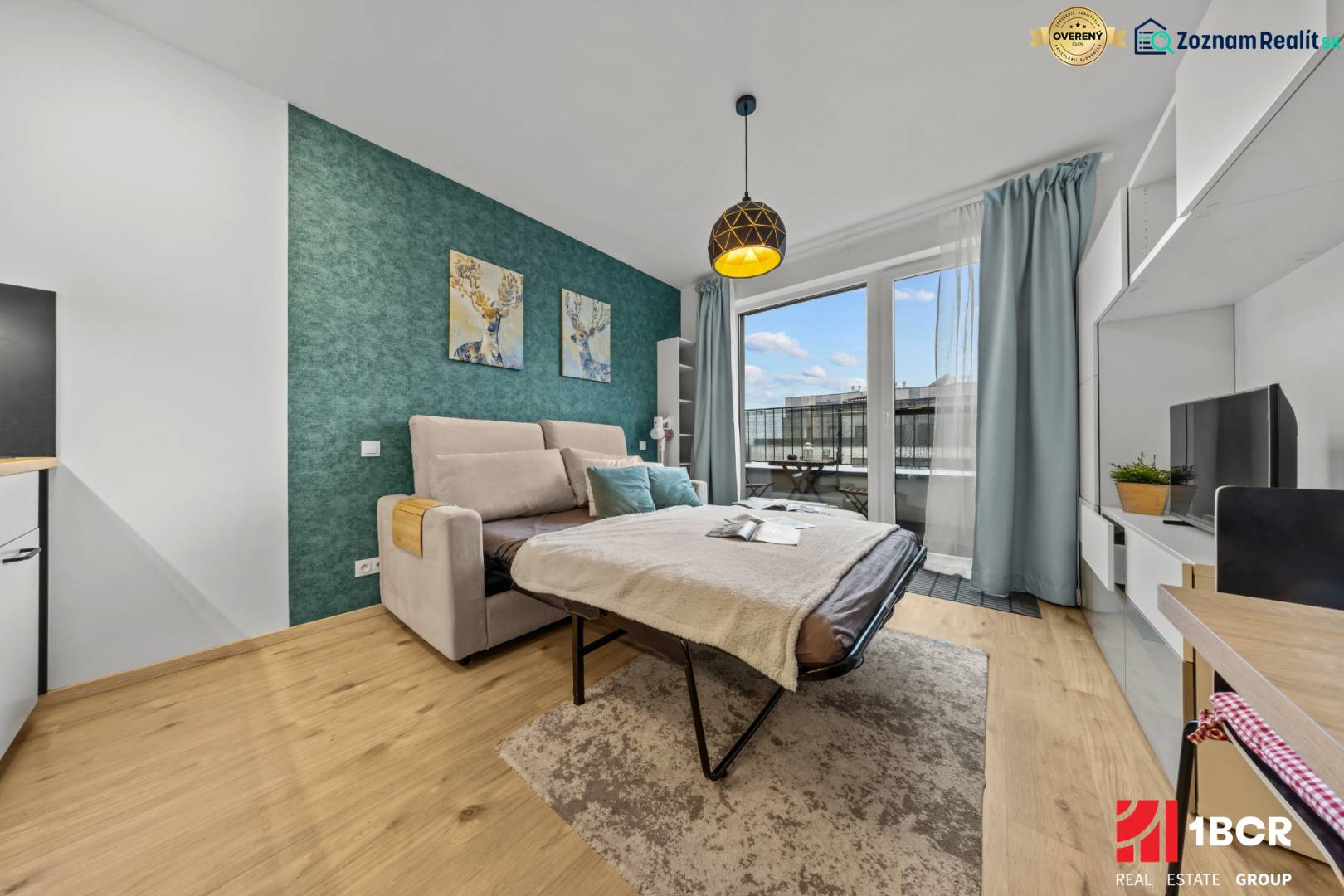 ZARIADENÝ 1-IZBOVÝ BYT, SLNEČNICE – IDEÁLNA INVESTÍCIA AJ BÝVANIE - Jednoizbový byt s rozkladacou pohovkou, balkónom, zelenou stenou a podlahou s dreveným dekorom.