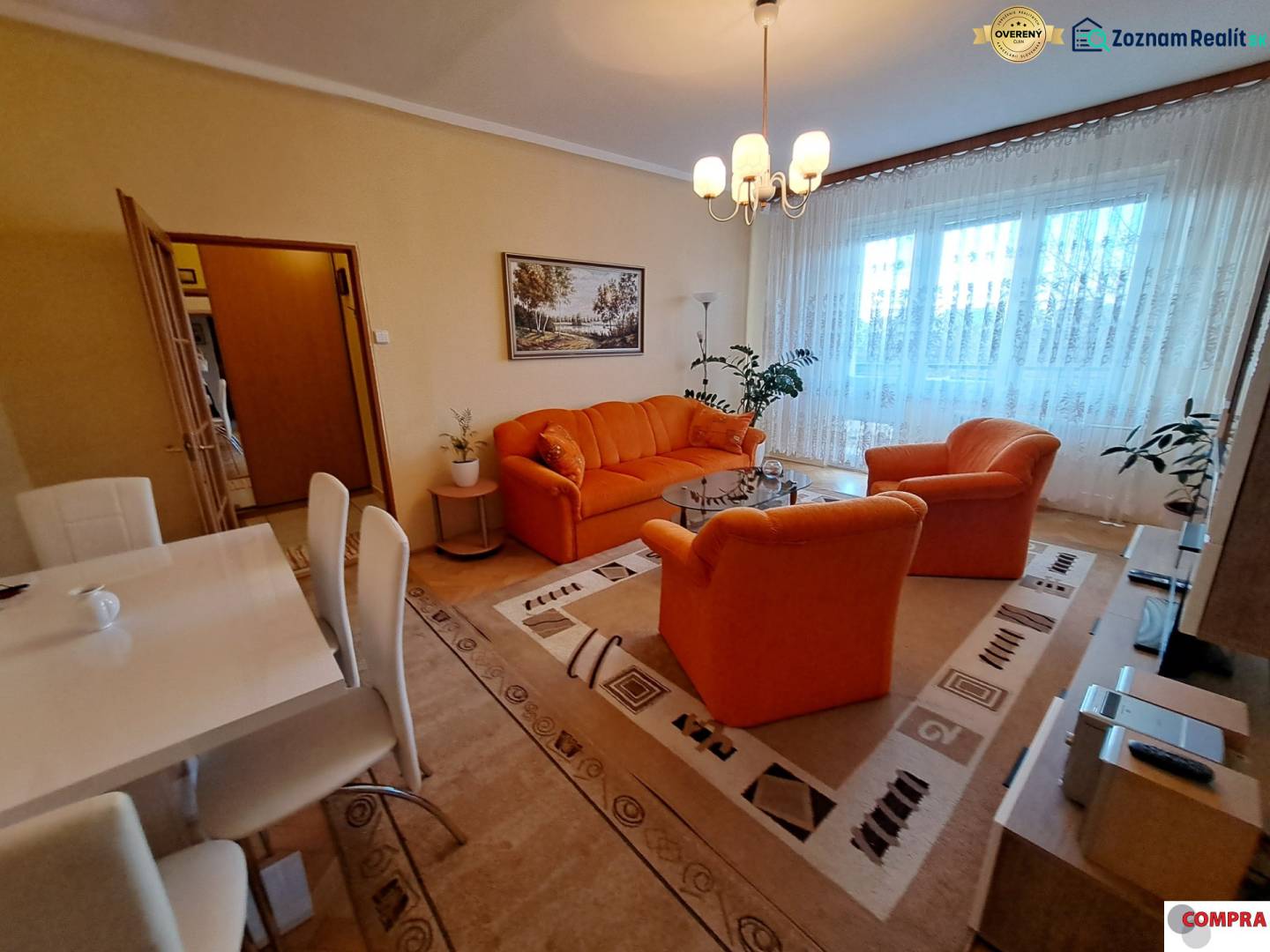 Pekný 2 izbový byt na Jadrovej ul. - Obývačka v 2-izbovom byte s oranžovým sedením, podlahou s dreveným dekorom a jedálenským stolom.