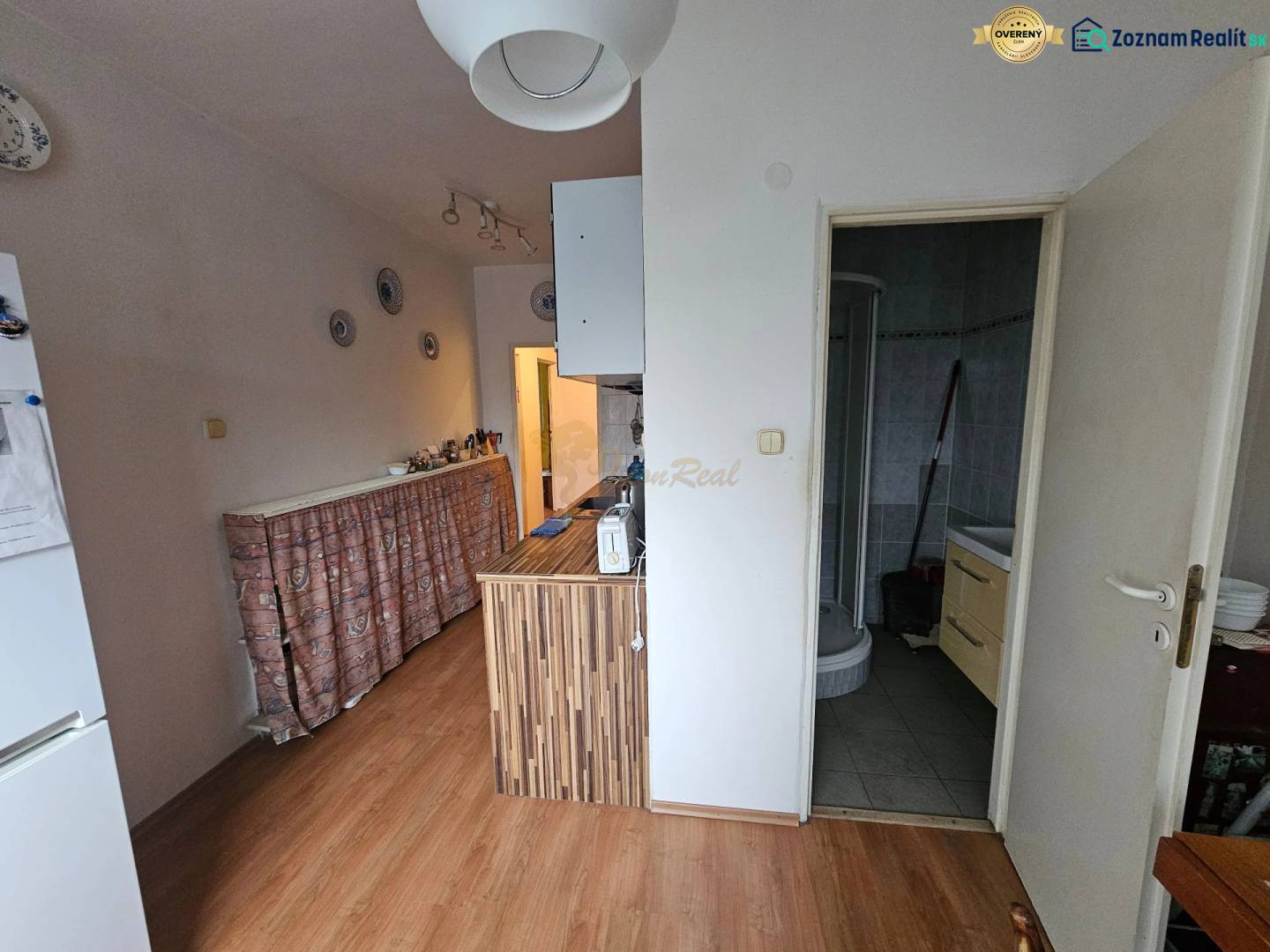 Veľký 2-izb. byt na ul. Nezábudková, Ružinov pri OC Retro - Kuchyňa v 2-izbovom byte s podlahou s dreveným dekorom a vstupom do kúpeľne.