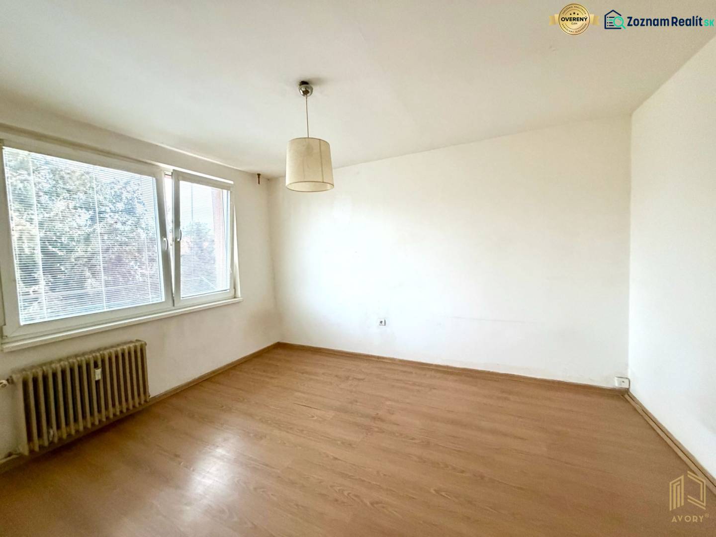 NA PREDAJ 1-IZB. BYT (28m2), BRATISLAVSKÁ UL., HOLÍČ - 1-izbový byt s veľkým oknom, podlaha s dreveným dekorom, biela stena, radiátor.