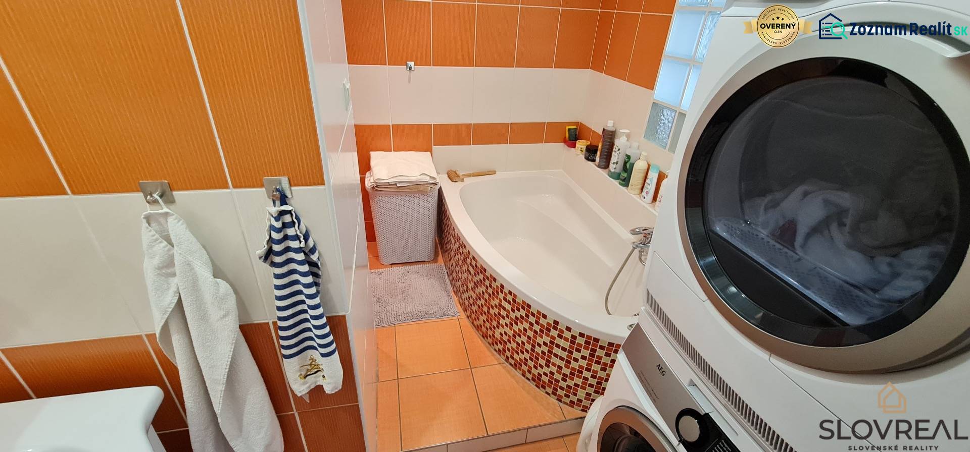 Predaj 2i byt v meste Kremnica, 64m2 - Kúpeľňa s vaňou a práčkou v 2-izbovom byte s oranžovými obkladačkami.