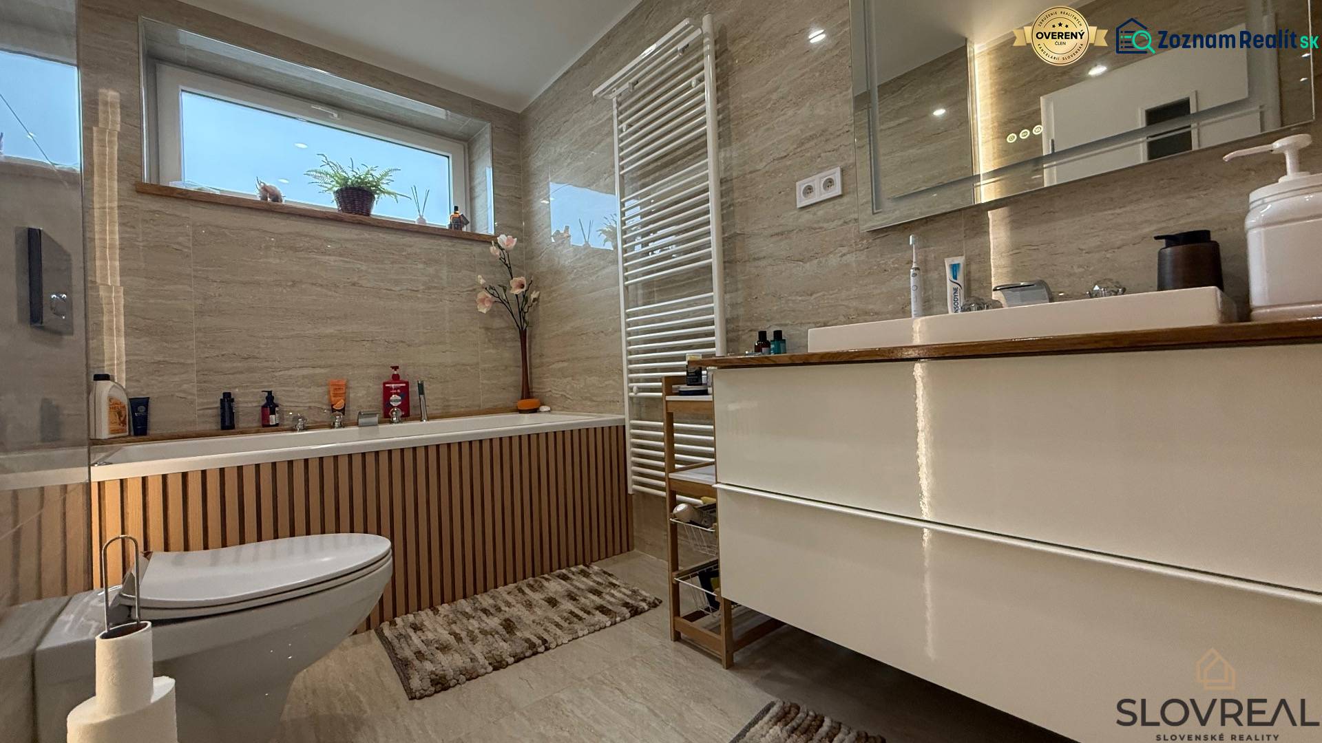 Rodinný dom v Bratislave – Podunajské Biskupice - Kúpeľňa v rodinnom dome s vaňou, umývadlom a oknom. Dekor dreva na stene.