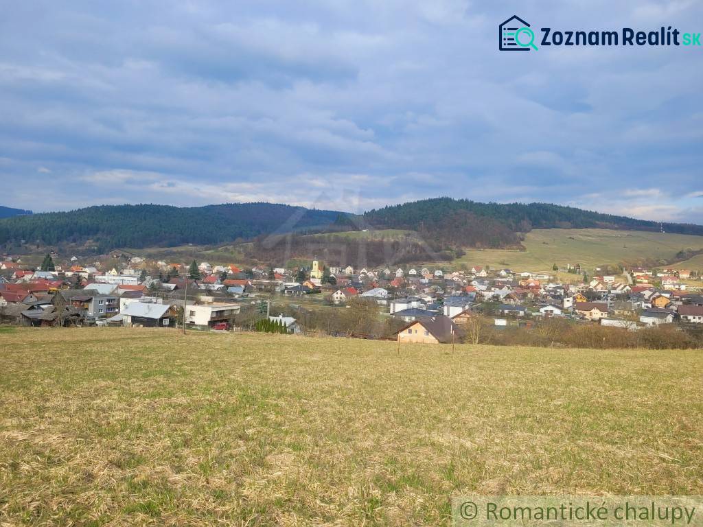 Stavebný pozemok s krásnym výhľadom nad obcou Jasenica pri Považskej B - Panoráma Jasenice so záhradami, obklopená políami a lesmi pod modrou oblohou.