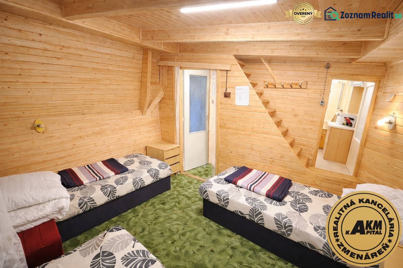 PRIPRAVUJEME Rekreačná chata - Zvolen - Kováčová na Predaj - Súčasťou interiéru chaty sú dve postele, drevené obklady a zelený koberec.