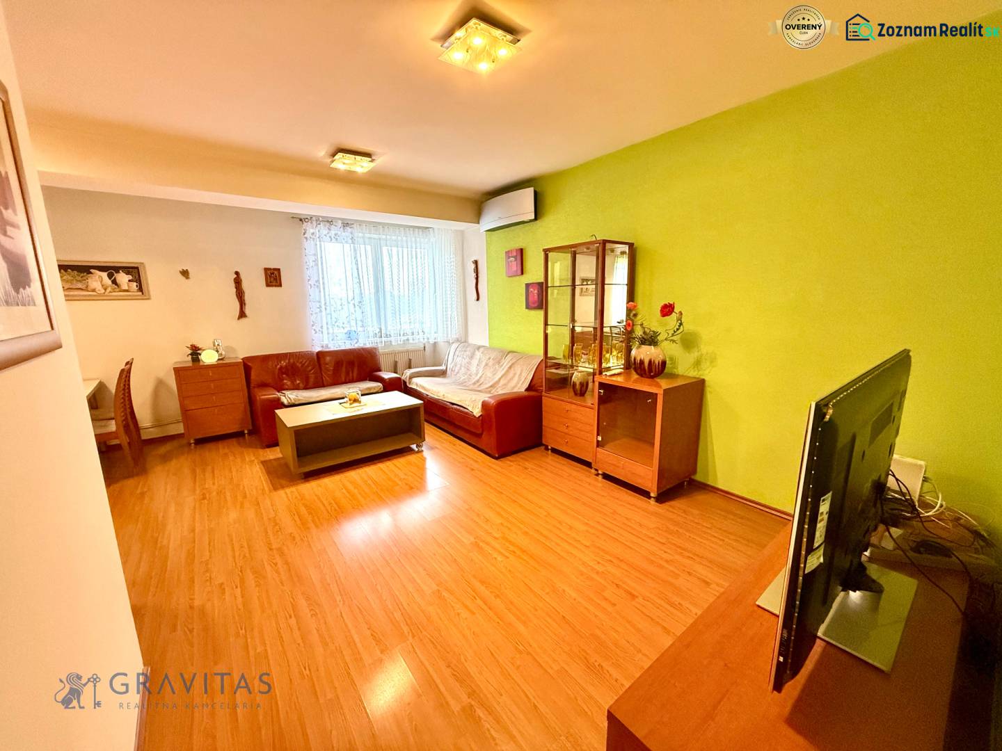 Na predaj – svetlý 2-izbový byt s loggiou a garážou | Bratislava - Obývacia izba s podlahou s dreveným dekorom, koženou sedačkou a vitrínou v 2-izbovom byte.