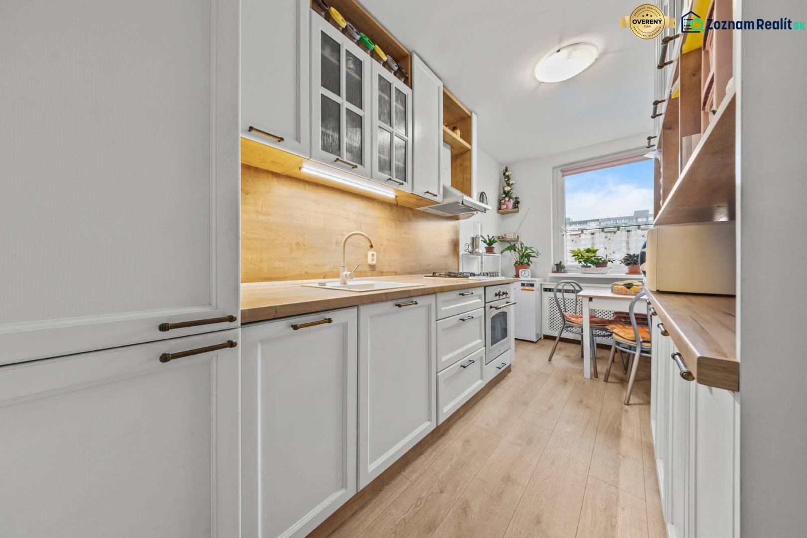 Ponúkame na predaj 3-izb.byt Vígľašská ul., Bratislava - Petržalka. - Kuchyňa v 3-izbovom byte s bielymi skrinkami, podlahou s dreveným dekorom a priestranným oknom.