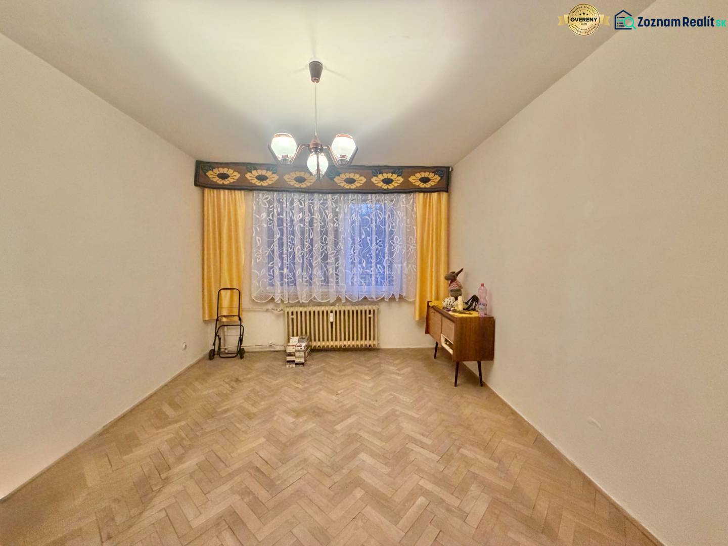 Predaj pôvodného 3+1 bytu v žiadanej lokalite v Čadci (MO) - Izba v 3-izbovom byte s podlahou s dreveným dekorom, záclonami a komodou.